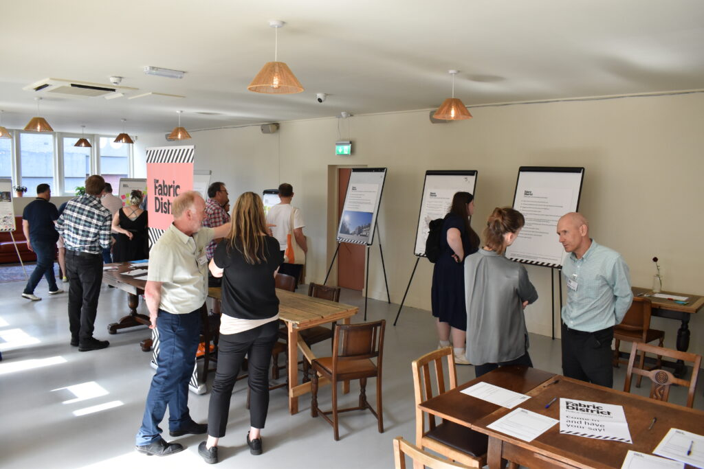 A photograph of members of the public looking at plans for the Fabric District and sharing their feedback.
